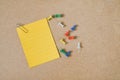 Yellow note paper with paper clip and multi color thumbtacks on brown grunge board, top view Royalty Free Stock Photo