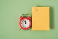 Yellow note paper with paper clip and red analog alarm clock on green background Royalty Free Stock Photo