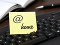 yellow note with at sign and the text, home, on a black keyboard at the desk at home, concept for home office Royalty Free Stock Photo