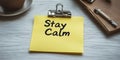 Yellow Note with Stay Calm Message, Coffee Cup, and Notepad on a White Wooden Table Royalty Free Stock Photo