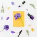 Yellow notebook, blue anemones with nail polish and lipstick on white. Flat lay