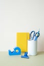 Yellow notebook, blue colored pencil, pen, scissors, clip, tape dispenser on desk. white ivory background. workspace office