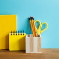 Yellow notebook, pencil holder, scissor, ruler on wooden desk. blue wall background Royalty Free Stock Photo