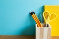 Yellow notebook, pencil holder, scissor, ruler on wooden desk. blue wall background Royalty Free Stock Photo