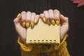 Yellow notepad in female hands. Manicure with a pattern. Close-u