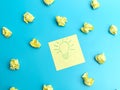 Yellow notepaper with a painted burning lamp lies on a blue background between crumpled pieces of paper. . The concept of the