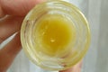 Yellow ointment in a transparent round jar . Held by the left hand . Ugly Butter disgusting substance . Beauty product treatment