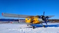 A yellow old biplane plane is parked on a winter airfield against a background of bright blue sky and white snow with the engine r Royalty Free Stock Photo