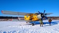 A yellow old biplane plane is parked on a winter airfield with technicians at work against a bright blue sky and white snow Royalty Free Stock Photo