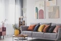 Yellow, orange, black and brown pillows on comfortable grey scandinavian sofa in bright living room interior with abstract Royalty Free Stock Photo