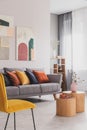 Yellow, orange, black and brown pillows on comfortable grey scandinavian sofa in bright living room interior with abstract