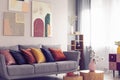 Yellow, orange, black and brown pillows on comfortable grey scandinavian sofa in bright living room interior with abstract