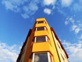 Yellow and orange building on a white clouds blue sky background. Minimalistic architecture stock photo, windows