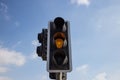 Yellow, orange color traffic light isolated. Blue sky with clouds background. Close up under view.