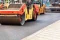 Construction of a new road, road rollers compacting fresh asphalt on the road immediately following the pavers on a summer day
