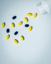 Yellow oval tablet pills and black tablets pills spilling out of pill bottle on white background with copy space for text. Global Royalty Free Stock Photo