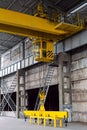 Yellow overhead crane with linear traverse and hooks in engineering plant workshop