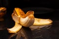 Yellow overripe half peeled banana on black background. Ripening organic fruit. Dark low key. Close up. Selective focus. Blurred Royalty Free Stock Photo