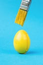 Yellow paint dripping from a yellow brush onto a yellow egg on a blue background. The concept of the Easter meeting Royalty Free Stock Photo