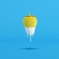 Yellow painted strawberry dripped in white paint on blue background