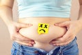 A yellow paper blank message is drawn: a sad face on belly fat with hands squeezes at the waist of a young woman in jeans. Royalty Free Stock Photo
