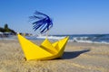 Yellow paper boat with cocktail stick decoration on sandy seashore with sea Royalty Free Stock Photo