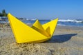 Yellow paper boat on sand on seashore against backdrop of sea waves Royalty Free Stock Photo