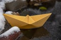 Yellow paper boat stuck in the ice, on a frozen puddle Royalty Free Stock Photo