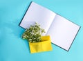 Yellow paper envelope with small garden white chamomile flowers and empty notepad on light blue background. Festive floral templat