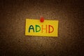 A yellow paper note with the abbreviation ADHD on it pinned to a cork board