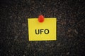 A yellow paper note with the abbreviation UFO on it pinned to a cork board