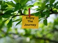 A yellow paper note with the phrase Enjoy the Journey on it attached to a tree branch with a clothes pin