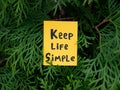 A yellow paper note with the phrase Keep Life Simple on it hanging on a arborvitae tree