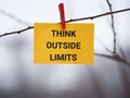 A yellow paper note with the phrase Think Outside Limits on it attached to a tree with a clothes pin