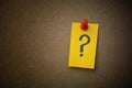 A yellow paper note with a question mark on it pinned to a cardboard background