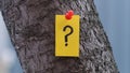 A yellow paper note with a question mark on it pinned to a tree.