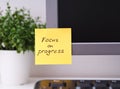 Yellow paper note with reminder Focus on Progress on it sticked on to a monitor