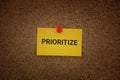 A yellow paper note with the word Prioritize on it pinned to a cork board Royalty Free Stock Photo