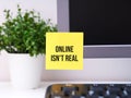 Yellow paper note with words Online isn\'t Real sticked on to a monitor at an office workplace