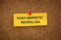 A yellow paper note with the words Post-Herpetic Neuralgia on it pinned to a cork board
