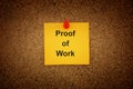 A yellow paper note with the words Proof of Work on it pinned to cork board