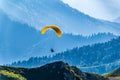 Yellow paraglider fly over mountain slope on sunny summer day