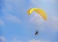 A yellow paraglider with a paramotor, soaring in the rays of the evening sun.