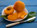 Yellow peaches full and cut on white plate with green leaves, on blue table. Closeup, fruits Royalty Free Stock Photo