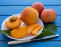 Yellow peaches full and cut on white plate with green leaves, on blue table. Closeup, fruits Royalty Free Stock Photo