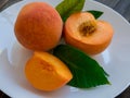 Yellow peaches full and cut on white plate with green leaves, on wooden table. Closeup, fruits Royalty Free Stock Photo