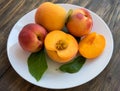 Yellow peaches full and cut on white plate with green leaves, on wooden table. Closeup, fruits Royalty Free Stock Photo