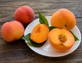 Yellow peaches full and cut on white plate with green leaves, on wooden table. Closeup, fruits Royalty Free Stock Photo