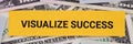 A yellow piece of paper with the phrase Visualize Success lying on a pile of dollar bills