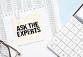 a yellow piece of paper with the text Ask the Expert and the calculator are lying on the notepad Royalty Free Stock Photo
